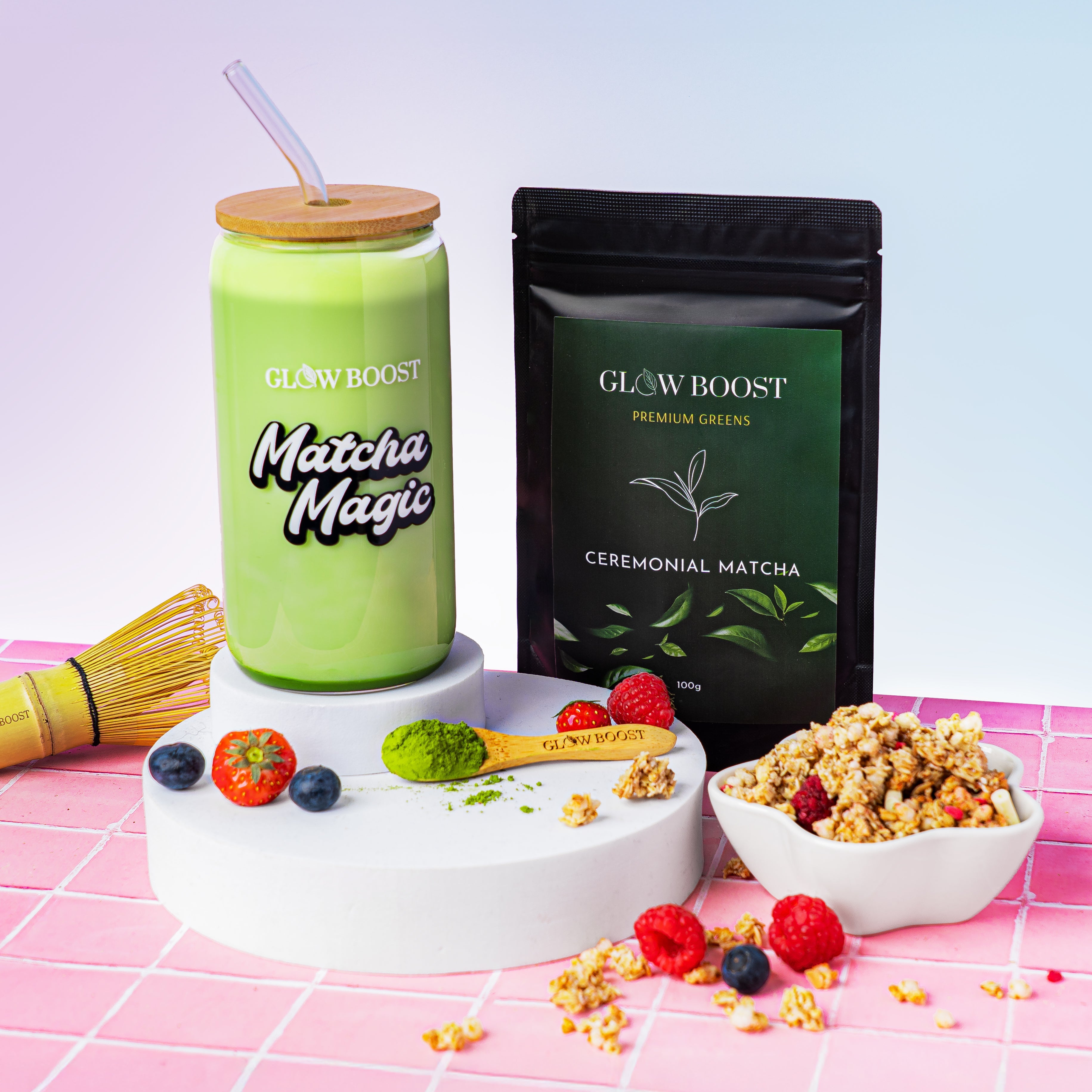 Matcha Magic drink with a straw, Glowboost Ceremonial Matcha packaging, and granola on a pink grid background.